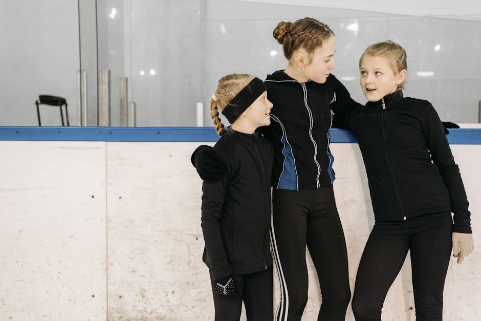Three young female ice skaters in black jackets standing together at an indoor rink.