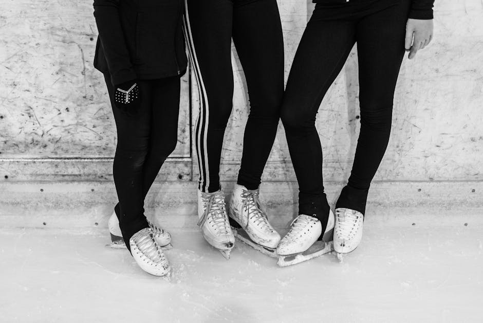 Close-up black and white image capturing three people in ice skates and leggings at an ice rink.